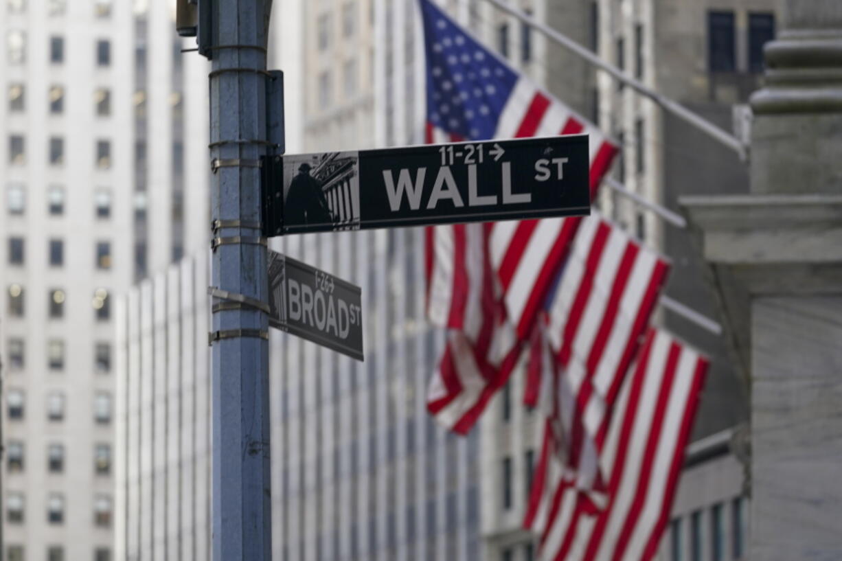 FILE - The Wall St. street sign is framed by the American flags flying outside the New York Stock exchange, Friday, Jan. 14, 2022, in the Financial District. Stocks wavered between small gains and losses in morning trading on Wall Street Wednesday, Feb. 23,  as the crisis in Ukraine remains tense.