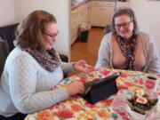 Helen Rottier, 25, shows her mother, Amy Rottier, 50, how she organizes her calendar on her iPad while sitting at the dining room table of her family's home in Madison, Wis., on Wednesday, Jan. 26, 2022. The two women illustrate the way Gen Xers and millennials differ in how they spent their time on an average day as young adults because of changes in technology and patterns in forming families over the last two decades. (AP Photo/Scott Bauer).