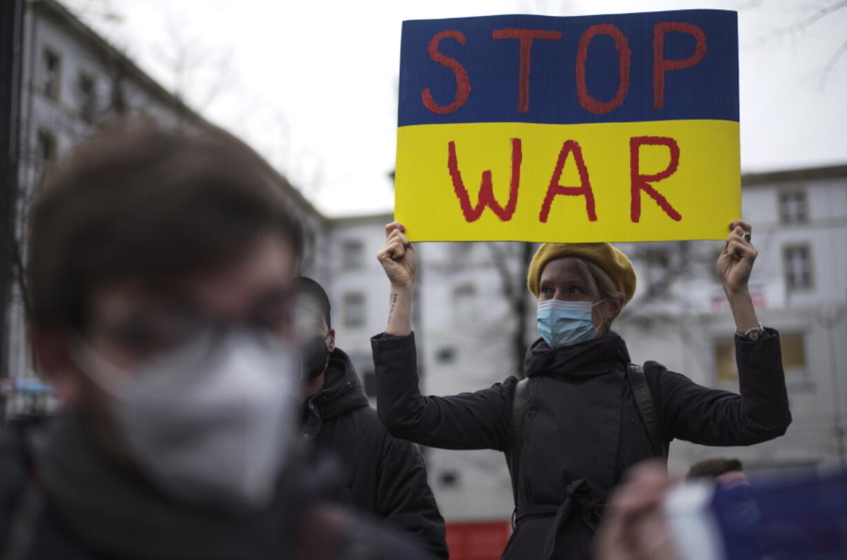 A woman with a poster attends a demonstration along the street near the Russian embassy to protest against the escalation of the tension between Russia and Ukraine in Berlin, Germany, Tuesday, Feb. 22, 2022. Lawmakers gave Russian President Vladimir Putin permission to use military force outside the country on Tuesday. The move that could presage a broader attack on Ukraine after the U.S. said an invasion was already underway there.