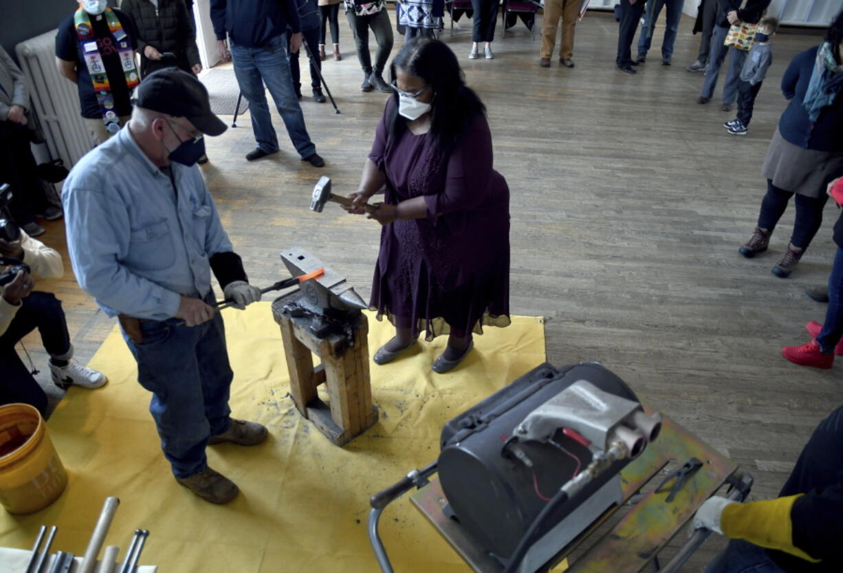 Sharletta Evans, right, whose 3-year-old son, Casson, was killed in a drive-by shooting in 1995, helps Fred Martin, a volunteer blacksmith for the nonprofit group RAWtools, hammer a rifle barrel into a garden tool at a church in Denver, Sunday, Jan. 16, 2022.