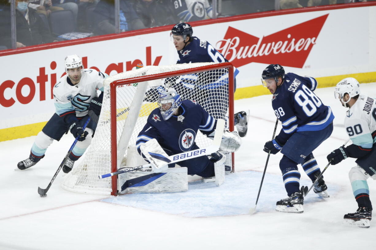 Seattle Kraken's Jordan Eberle (7) looks for Marcus Johansson (90) as he attempts to make a pass in front of Winnipeg Jets goaltender Eric Comrie (1) during the second period of an NHL hockey game Thursday, Feb. 17, 2022 in Winnipeg, Manitoba.