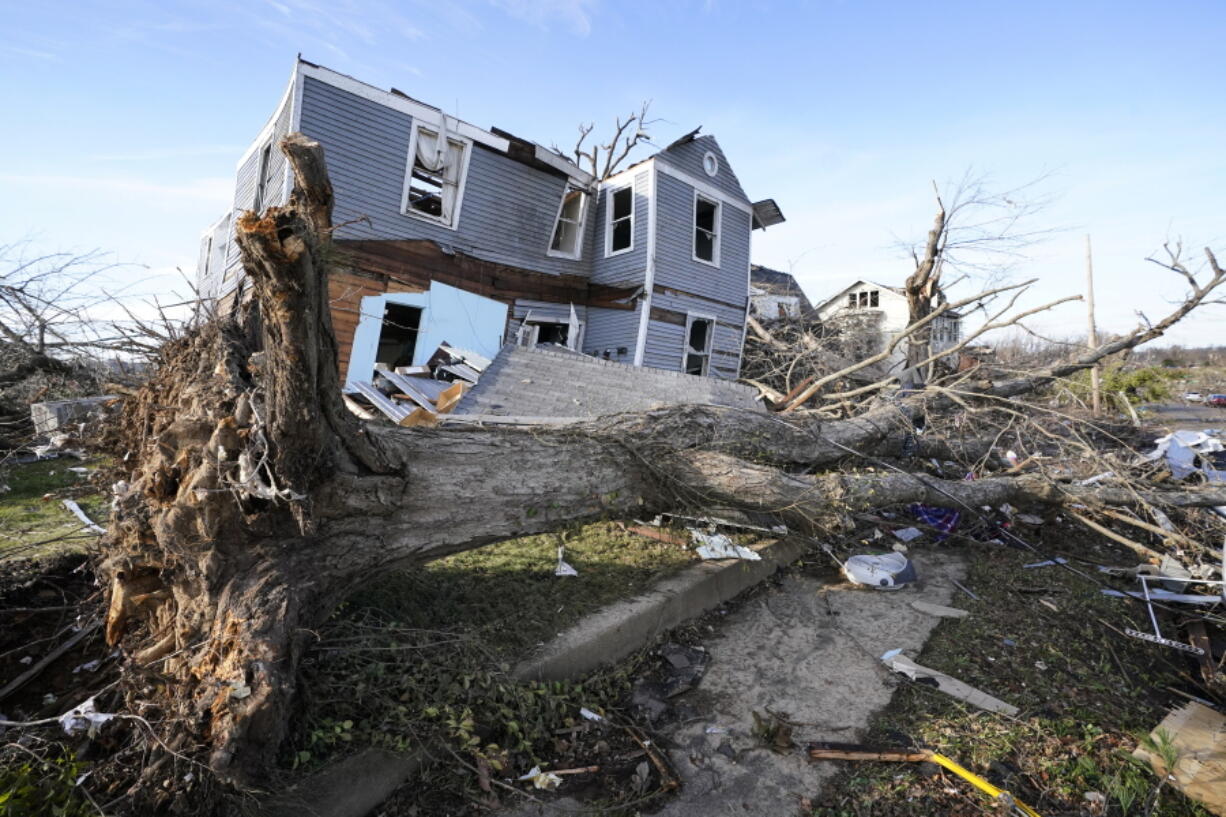 An overturned tree sits in front of a tornado-damaged home in Mayfield, Ky., on Dec. 11. Kentucky's death toll from tornadoes in December has risen. On Monday, Kentucky Gov. Andy Beshear announced the deaths of a woman and her infant.