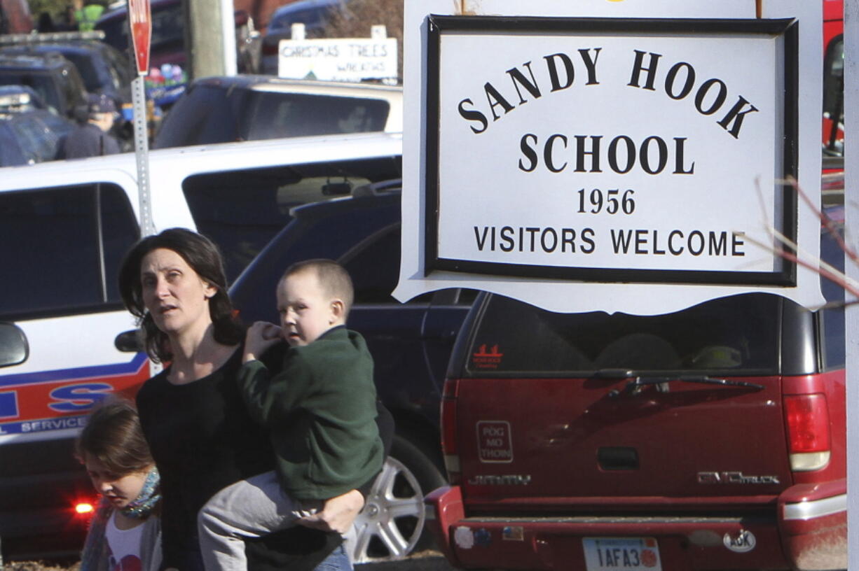 FILE -- A parent walks away from the Sandy Hook Elementary School with her children following a shooting at the school in Newtown, Conn., Dec. 14, 2012. The families of nine victims of the Sandy Hook Elementary School shooting have agreed to a settlement of a lawsuit against the maker of the rifle used to kill 20 first graders and six educators in 2012, according to a court filing, Tuesday, Feb. 15, 2022.