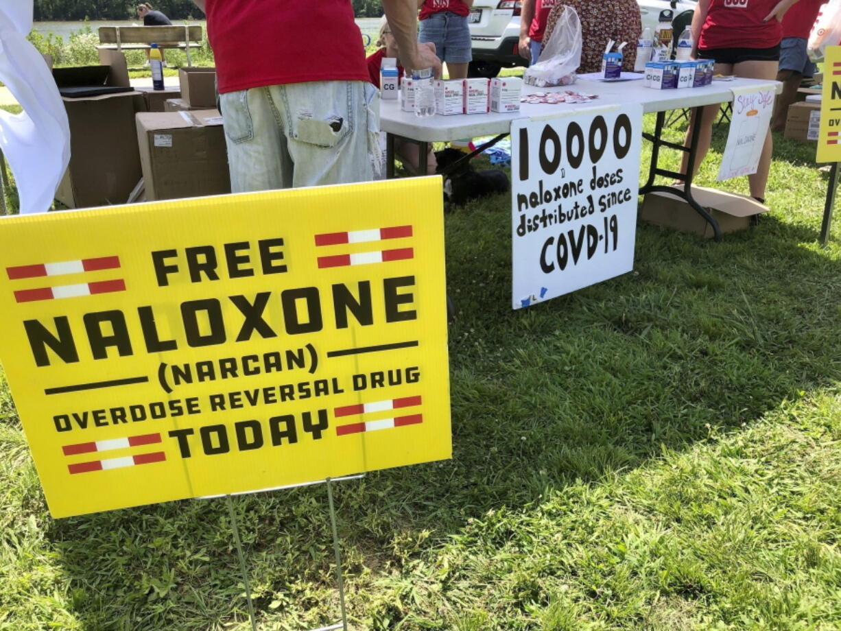 FILE - Signs are displayed at a tent during a health event on June 26, 2021, in Charleston, W.Va. Volunteers at the tent passed free doses of naloxone, a drug that reverses the effects of an opioid overdose by helping the person breathe again. The U.S. needs a more nimble strategy and Cabinet-level leadership to counter its festering opioid epidemic, a bipartisan congressional commission said Tuesday.