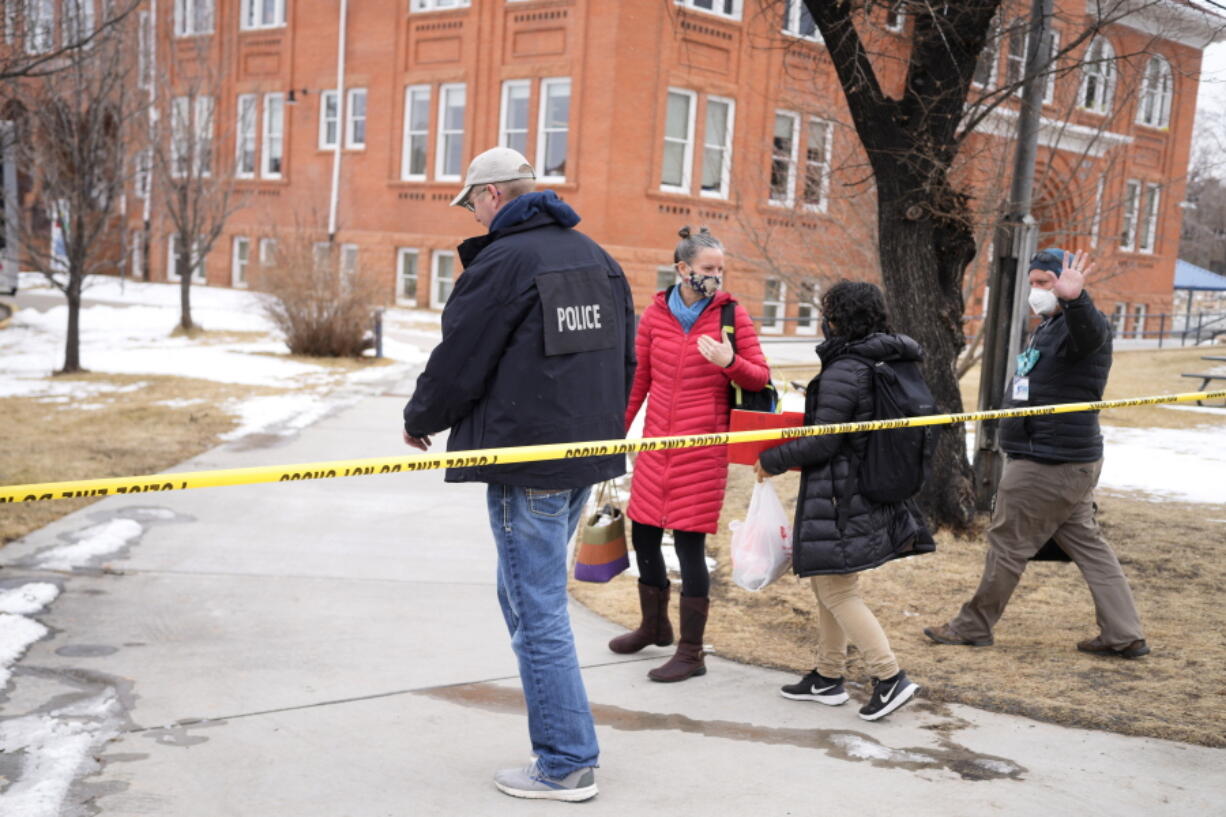 Police officer escorts people past a police line in front of University Hill Elementary School across from the campus of the University of Colorado after a man accused of making mass shooting threats against the college as well as the University of California, Los Angeles, was arrested Tuesday, Feb. 1, 2022, in Boulder, Colo. The police operation caused the evacuation of the elementary school and shelter-in-place orders for nearby residents on Boulder's University Hill.