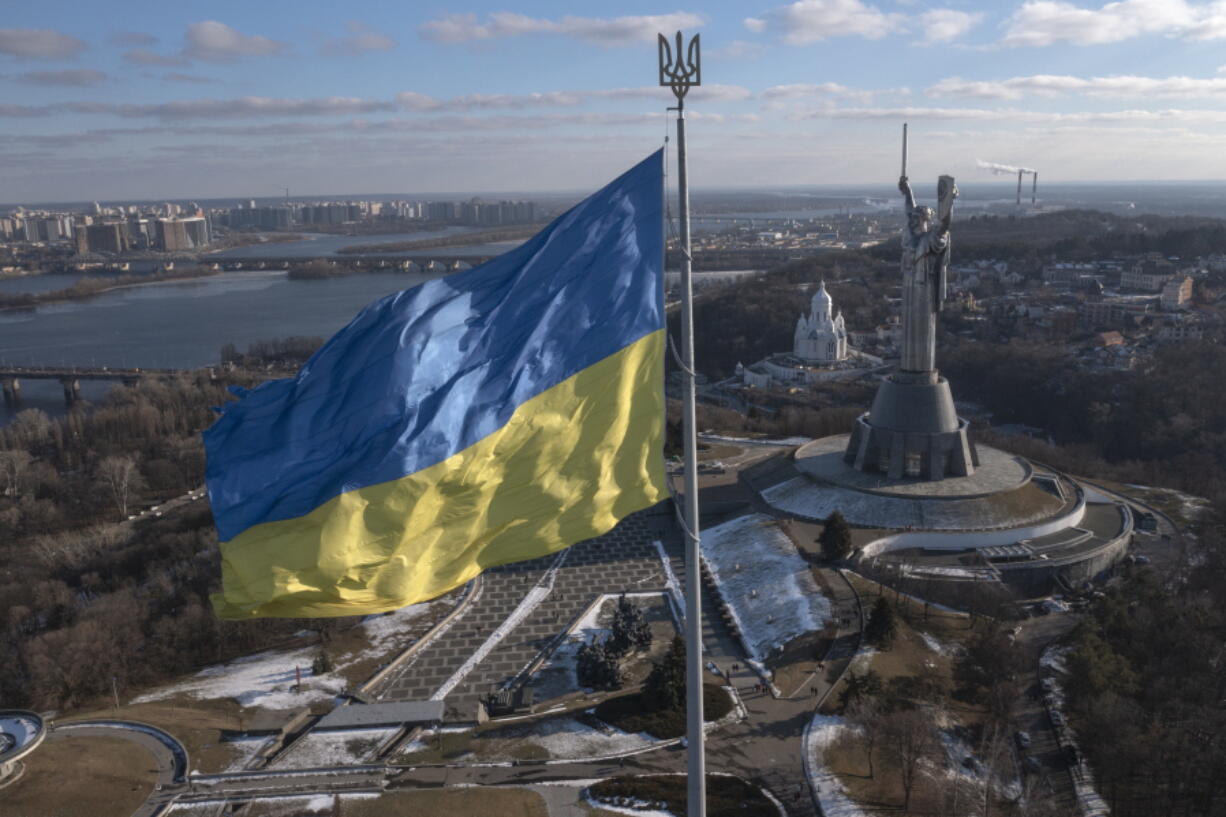 A view of Ukraine's national flag waves above the capital with the Motherland Monument on the right, in Kyiv Sunday, Feb. 13, 2022. Some airlines have halted or diverted flights to Ukraine amid heightened fears that an invasion by Russia is imminent despite intensive weekend talks between the Kremlin and the West.