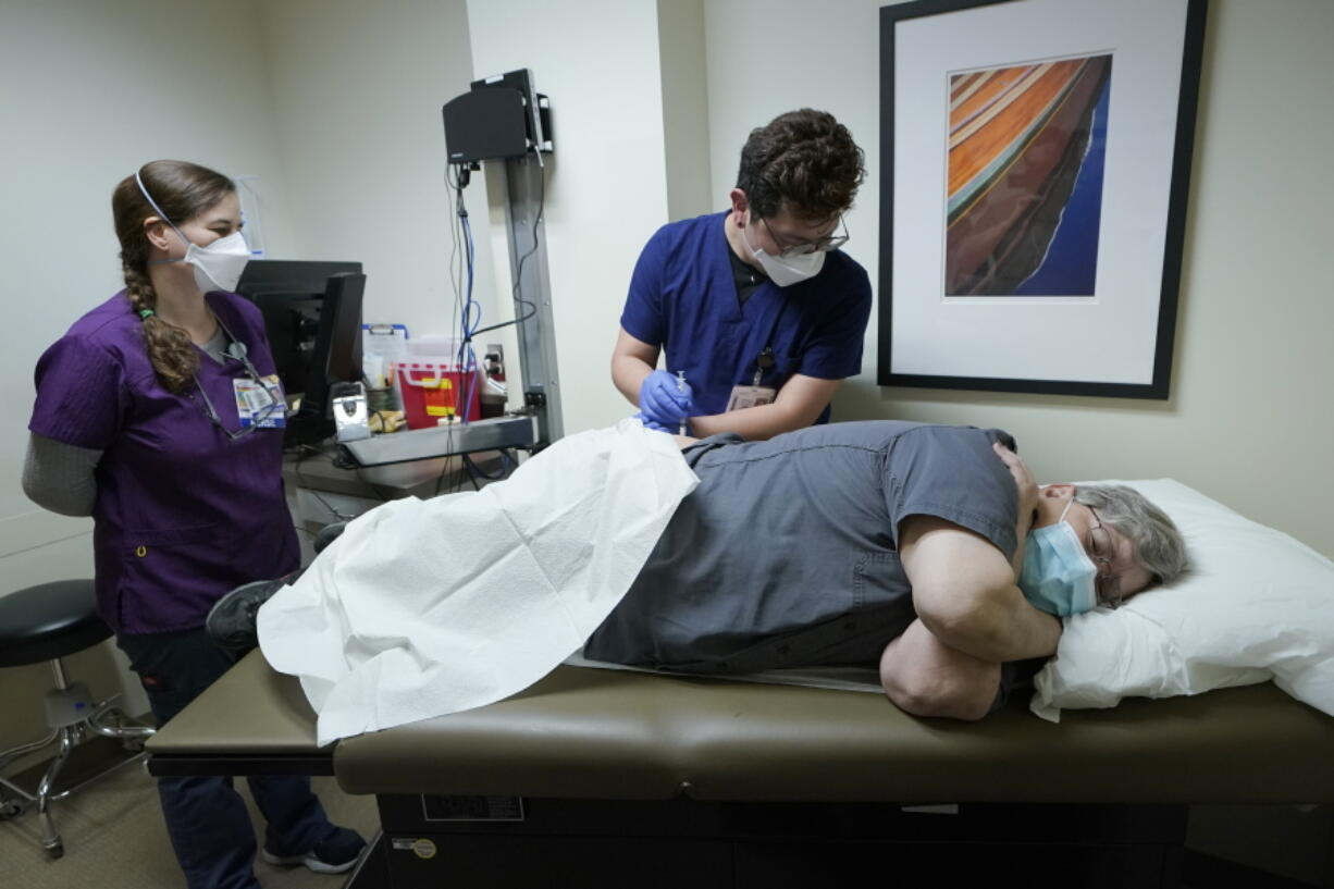 Ray Hoffman, right, who is immune-compromised, is given a shot of the two-shot dose of AstraZeneca's Evusheld -- the first set of antibodies grown in a lab to prevent COVID-19, Thursday, Jan. 20, 2022, by Jose Lazaro, center, a medical assistant at a University of Washington Medicine clinic in Seattle as Cynde Wiederhold, left, a nurse, looks on. The two-shot dose is supposed to give patients like Hoffman, who can't make his own virus-fighters due to taking strong immune-suppressing drugs after liver and kidney transplants, some protection against COVID-19 for six months. (AP Photo/Ted S.