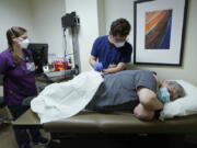 Ray Hoffman, right, who is immune-compromised, is given a shot of the two-shot dose of AstraZeneca's Evusheld -- the first set of antibodies grown in a lab to prevent COVID-19, Thursday, Jan. 20, 2022, by Jose Lazaro, center, a medical assistant at a University of Washington Medicine clinic in Seattle as Cynde Wiederhold, left, a nurse, looks on. The two-shot dose is supposed to give patients like Hoffman, who can't make his own virus-fighters due to taking strong immune-suppressing drugs after liver and kidney transplants, some protection against COVID-19 for six months. (AP Photo/Ted S.