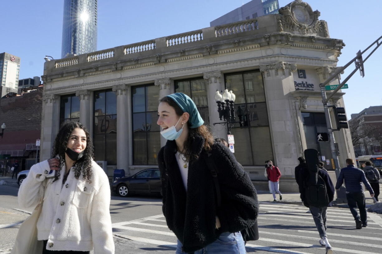 FILE - Passers-by wear masks under their chins as they chat with one another while crossing a street, in Boston, Wednesday, Feb. 9, 2022. Students and staff at public schools in Massachusetts will no longer be required to wear face coverings while indoors starting Feb. 28, state officials said Wednesday, Feb. 9, 2022.