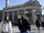 FILE - Passers-by wear masks under their chins as they chat with one another while crossing a street, in Boston, Wednesday, Feb. 9, 2022. Students and staff at public schools in Massachusetts will no longer be required to wear face coverings while indoors starting Feb. 28, state officials said Wednesday, Feb. 9, 2022.