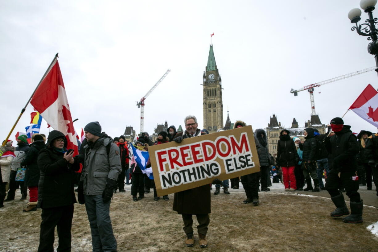 Don Stephens, 65, a retired graphic designer, holds a sign on Parliament Hill to support trucks lined up in protest of COVID-19 vaccine mandates in Ottawa, Ontario, on Saturday, Feb. 12, 2022. Protesters opposed to COVID-19 vaccine mandates and other restrictions have withdrawn their vehicles from a key U.S.-Canadian border bridge but ramped up demonstrations in cities across Canada.