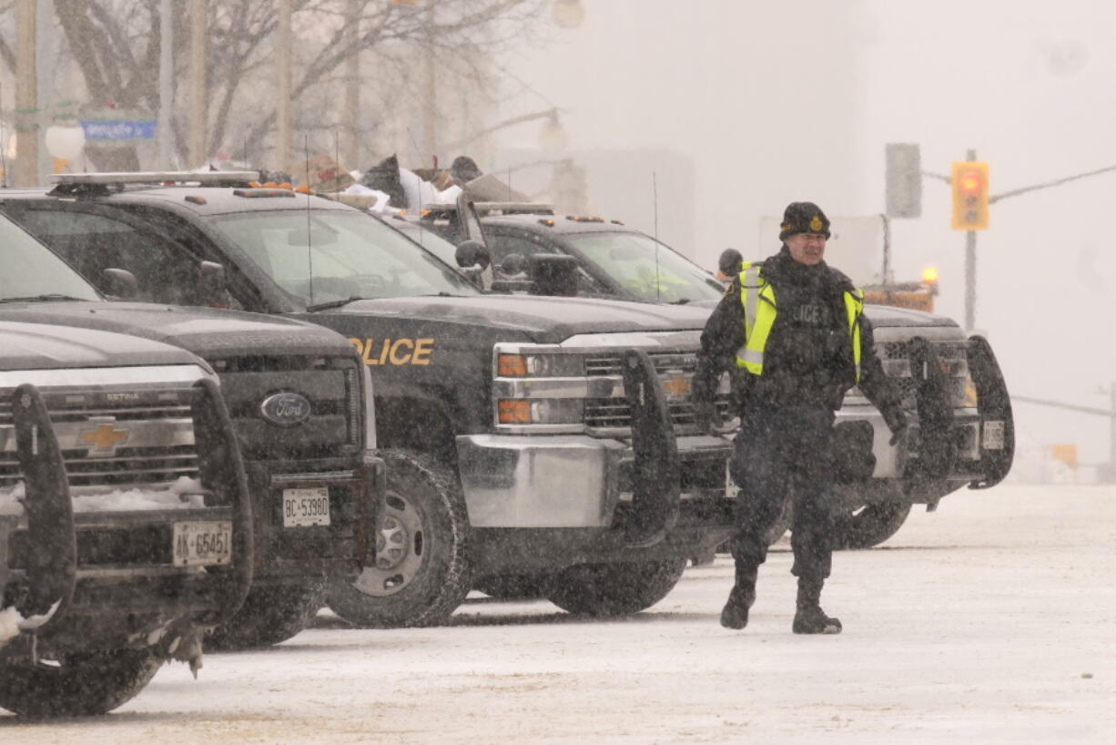 An officer stands next to police vehicles are parked downtown Ottawa on Sunday, Feb. 20, 2022. A protest, which was first aimed at a COVID-19 vaccine mandate for cross-border truckers but also encompassed fury over the range of COVID-19 restrictions.