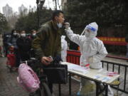 A man holding his bicycle with a school bag on it gets a throat swab during a mass COVID-19 test at a residential compound in Wuhan in central China's Hubei province, Tuesday, Feb. 22, 2022. Wuhan, the first major outbreak of the coronavirus pandemic has reported more than dozen new coronavirus cases this week, prompting the authority to step up precautious measures.