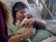 In this image provided by Kata Sasvari, Macenzee Keller, 20, of Manchester, N.H., clutches her two-month-old son Zachery for the first time since she giving birth, at the Dartmouth-Hitchcock Medical Center in Lebanon, N.H., Feb. 3, 2022. Keller delivered Zachery on Nov. 28, 2021, while on a ventilator at Catholic Medical Center in Manchester. N.H., after being stricken with COVID-19.