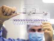 FILE - In this photo provided by Pfizer, a technician inspects filled vials of the Pfizer-BioNTech COVID-19 vaccine at the company's facility in Puurs, Belgium in March 2021. COVID-19 vaccines are saving an untold number of lives but they can't stop the chaos when a hugely contagious new mutant bursts on the scene, leading people to wonder: Will we need boosters every few months? A new vaccine recipe? A new type of shot altogether?