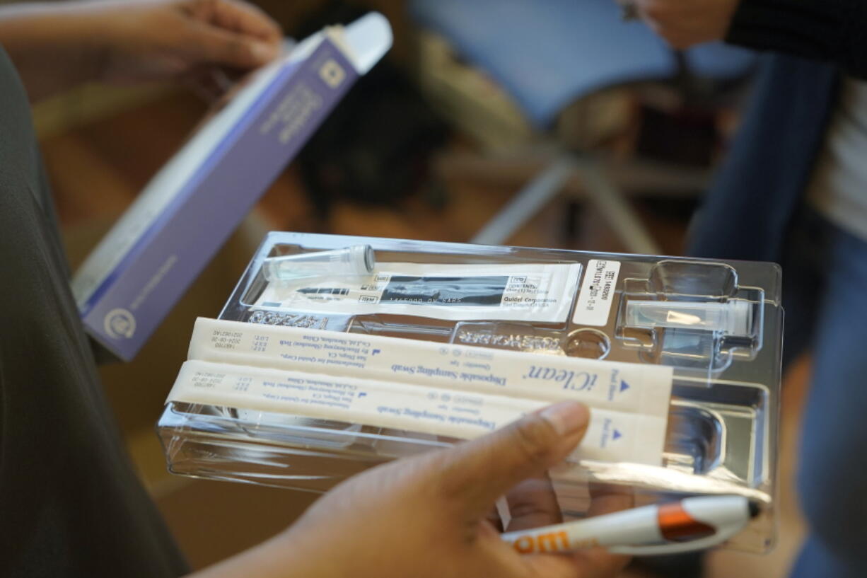 Kristin Travis, a community outreach doula, holds a home COVID-19 test kit Thursday, Feb. 3, 2022, while picking up supplies at Open Arms Perinatal Services before going out to visit some of her clients in Seattle. The kits were provided by the King County Public Health Dept. and distributed by community-based organizations as a way of providing more accessible testing and faster results. (AP Photo/Ted S.