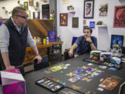 Orange Nebula creative director Marc Neidlinger, left, and president Tom Mattson talk about their board game Unsettled on Tuesday at the Orange Nebula office in Vancouver.  Game Informer, one of the most popular video game magazines, ranked Unsettled in the top 10 games of 2021. At top, a game piece from Unsettled.