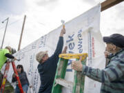 Construction began this week on nine homes at Evergreen Habitat for Humanity's Johnson Village, a plot of land in east Vancouver recently acquired by the organization. Those homes will all be owned by the Habitat Home Trust, a program launched by the organization that aims to create and preserve affordable housing stock in Clark County using a community land trust model. In this photo, Bill Lanavan, center, of Vancouver, staples a segment of Tyvek HomeWrap while CJ Joyce, right, of Vancouver, holds a ladder on Friday at the construction site.