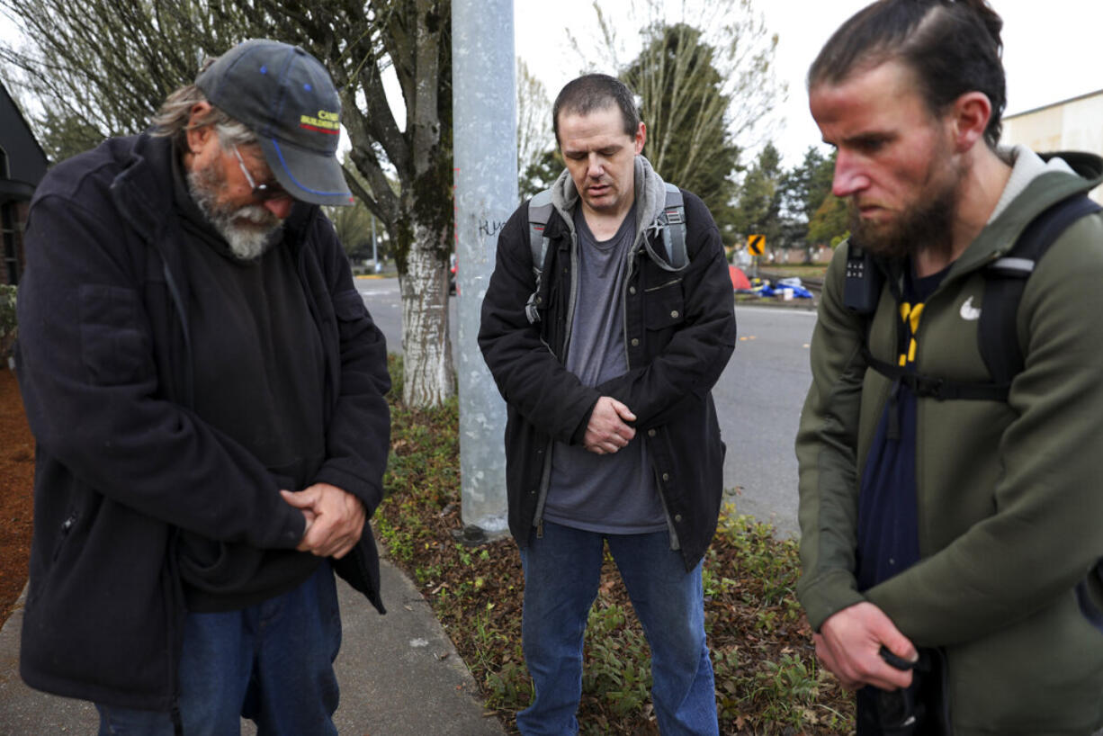 Carl Rhymes, Enoch Gerber and Mike Wade pray for the victims of a car accident that killed several people at a homeless camp near Front Street Northeast, Sunday, March 27, 2022, in Salem, Ore.