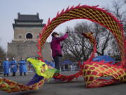 Community workers wearing protective suits watch over a masked resident twirling a dragon shaped ribbon near a barricaded coronavirus testing site setup outside the Drum Tower, Wednesday, March 23, 2022, in Beijing, China. A fast-spreading variant known as "stealth omicron" is testing China's zero-tolerance strategy, which had kept the virus at bay since the deadly initial outbreak in the city of Wuhan in early 2020.