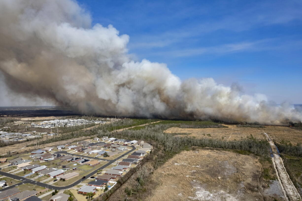 A fast-moving wildfire looms over homes outside of Panama City, Fla., Friday, March 4, 2022. More than 200 firefighters and emergency workers from throughout the Florida Panhandle worked overnight into Saturday, to strengthen containment lines and protect homes.