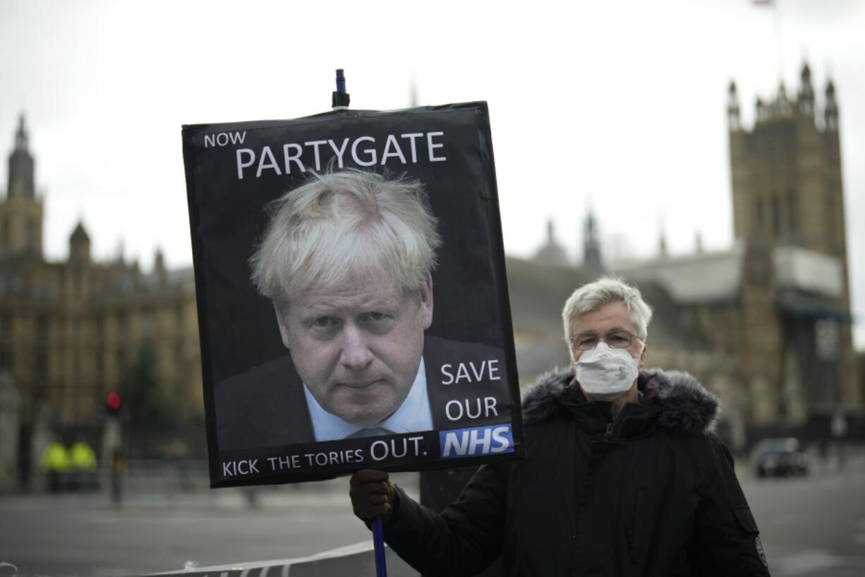 FILE - An anti-Conservative Party protester holds a placard with an image of British Prime Minister Boris Johnson including the words "Now Partygate" backdropped by the Houses of Parliament, in London, Wednesday, Dec. 8, 2021. British police are getting ready to issue a first batch of fines on over parties held by Prime Minister Boris Johnson's staff during coronavirus lockdowns. The Metropolitan Police declined to confirm reports multiple U.K. media outlets that fines would come as soon as Tuesday, March 29, 2022, saying it would not give "a running commentary" on its probe.