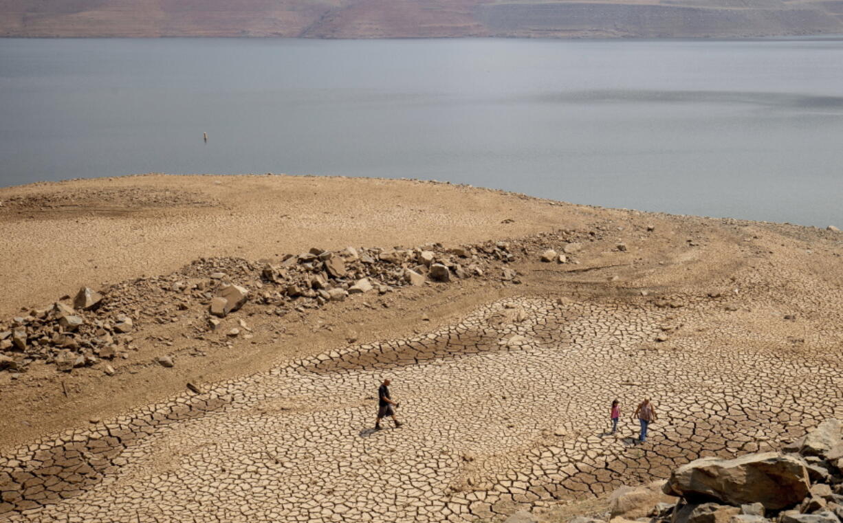 FILE -- In this Aug. 22, 2021, file photo, a family walks over cracked mud near Lake Oroville's shore as water levels remain low due to continuing drought conditions in Oroville, Calif. State water officials are preparing to tell major urban and agricultural water agencies on Friday, March 18, 2022, that they'll get even less water from state supplies than the small amount they were promised at the start of the year.