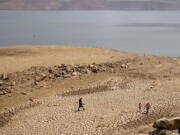 FILE -- In this Aug. 22, 2021, file photo, a family walks over cracked mud near Lake Oroville's shore as water levels remain low due to continuing drought conditions in Oroville, Calif. State water officials are preparing to tell major urban and agricultural water agencies on Friday, March 18, 2022, that they'll get even less water from state supplies than the small amount they were promised at the start of the year.