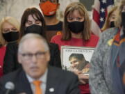 Kim Gatbunton, center, holds a photo of her son Josh Gatbunton, who was shot and killed during a 2008 robbery at an apartment in Tacoma, Wash., as she listens to Washington Gov. Jay Inslee, lower left, speak Wednesday, March 23, 2022, before signing a package of bills to tighten gun laws in Washington state at the Capitol in Olympia, Wash. (AP Photo/Ted S.