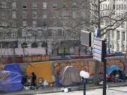 A person at left walks toward the entrance of a tent used by people experiencing homelessness, Tuesday, March 1, 2022, in downtown Seattle across the street from City Hall.  (AP Photo/Ted S.