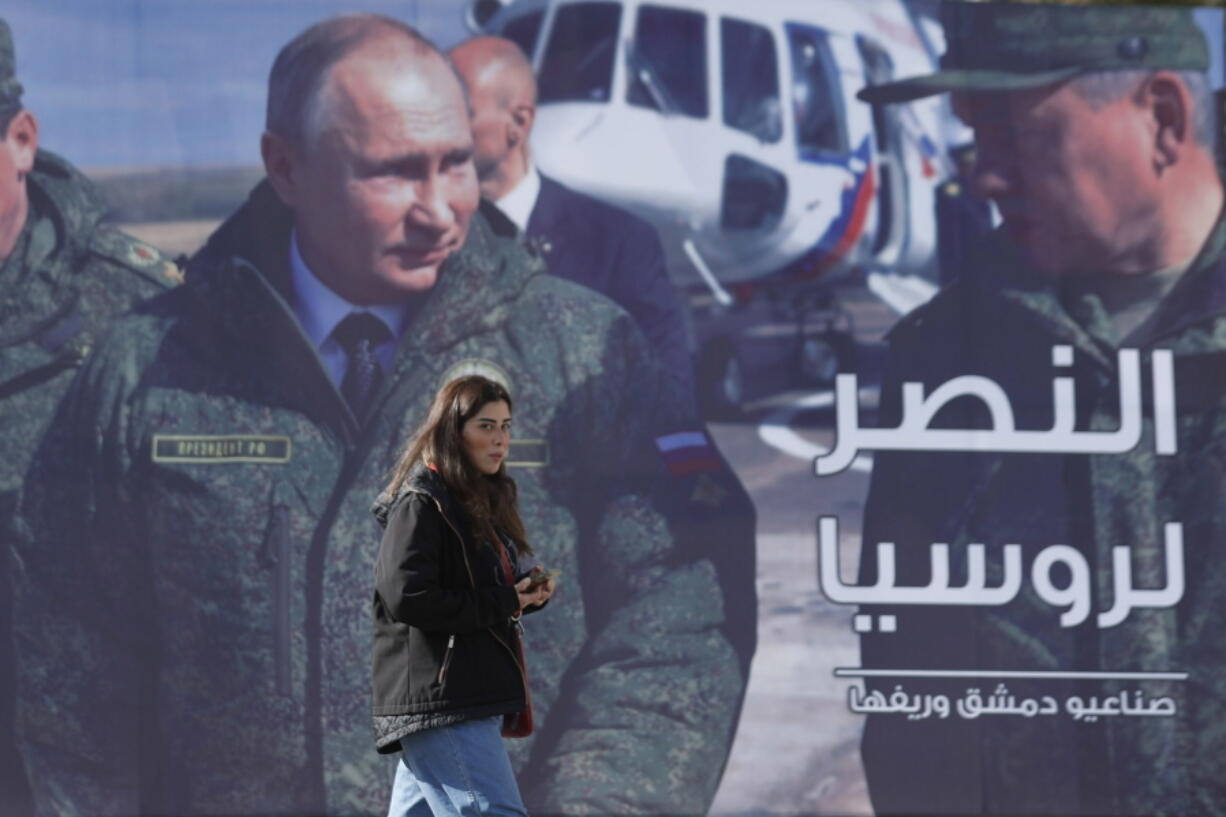 A woman passes a billboard showing Russian President Vladimir Putin in Damascus, Syria, Monday, March 7, 2022.