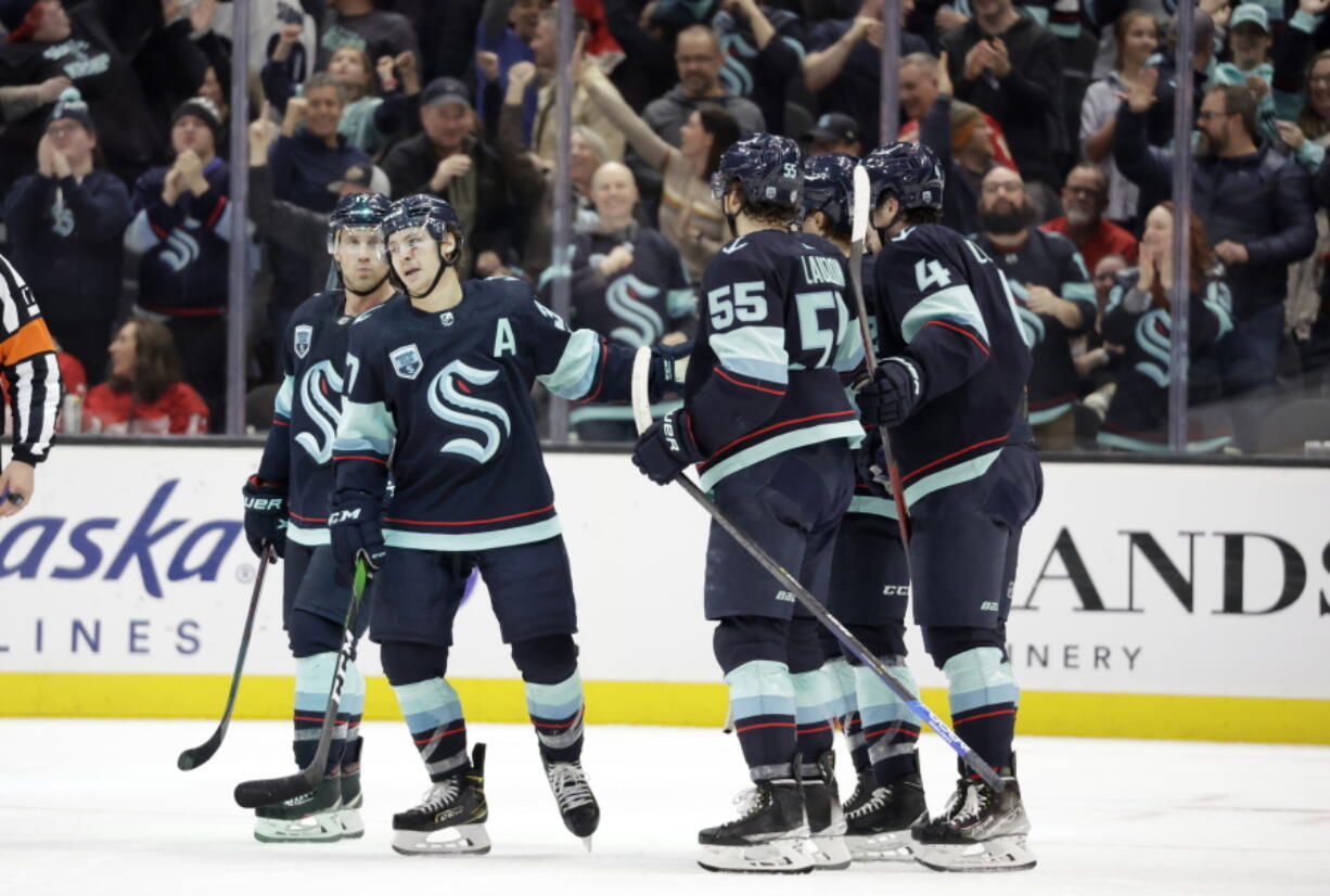 Seattle Kraken center Yanni Gourde, second from left, celebrates with center Jaden Schwartz, left, defenseman Jeremy Lauzon (55) and others after scoring the first of his two goals against the Detroit Red Wings during the third period of an NHL Hockey game Saturday, March 19, 2022, in Seattle. The Kraken won 4-2.