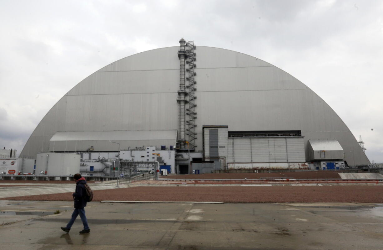 FILE - A man walks past a shelter covering the exploded reactor at the Chernobyl nuclear plant, in Chernobyl, Ukraine, Thursday, April 15, 2021. When fighting from Russia's invasion of Ukraine resulted in power cuts to the critical cooling system at the closed Chernobyl nuclear power plant, some feared that spent nuclear fuel would overheat. But nuclear experts say there's no imminent danger because time and physics are on safety's side.