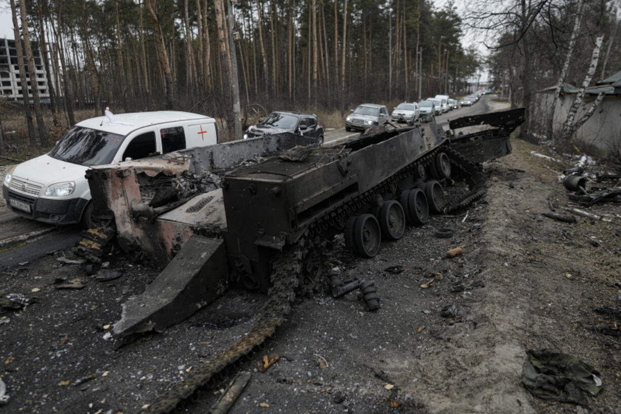 FILE - Cars drive past a destroyed Russian tank as a convoy of vehicles evacuating civilians leaves Irpin, on the outskirts of Kyiv, Ukraine, March 9, 2022. Thousands of patients in Ukraine are receiving lifesaving medicines to treat HIV and opioid addiction through a U.S.-funded group still operating despite the Russian invasion. Supplies are running short and making deliveries is a complicated calculus with unpredictable risks.