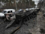 FILE - Cars drive past a destroyed Russian tank as a convoy of vehicles evacuating civilians leaves Irpin, on the outskirts of Kyiv, Ukraine, March 9, 2022. Thousands of patients in Ukraine are receiving lifesaving medicines to treat HIV and opioid addiction through a U.S.-funded group still operating despite the Russian invasion. Supplies are running short and making deliveries is a complicated calculus with unpredictable risks.