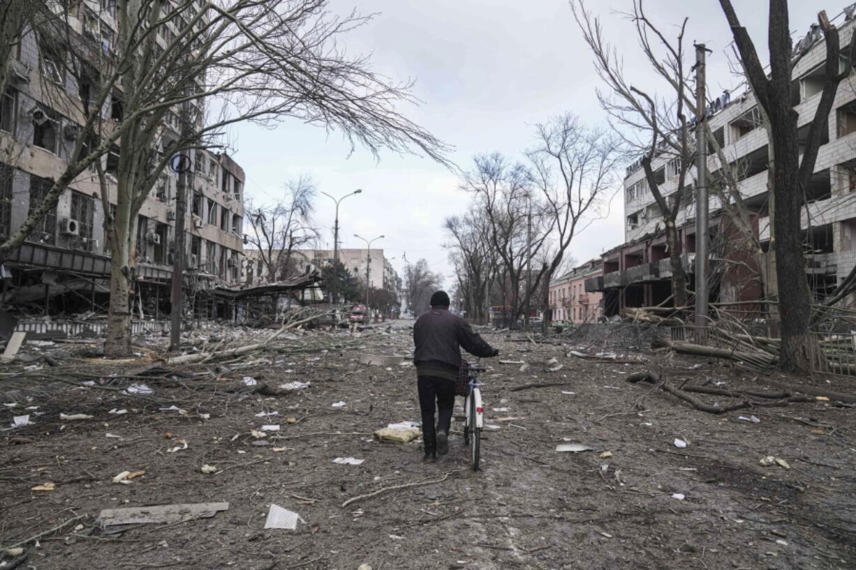 FILE - A man walks with a bicycle in a street damaged by shelling in Mariupol, Ukraine, March 10, 2022. In talks between Russia and Ukraine toward a possible cease-fire after three weeks of intense fighting, negotiators are exploring prospects of possible "neutrality" for Ukraine.