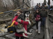 A woman holds a dog while crossing the Irpin River on an improvised path under a bridge as people flee the town of Irpin, Ukraine, on March 5.