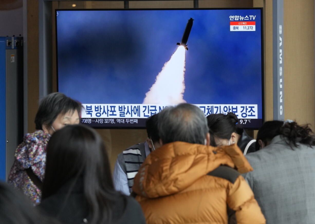 People stand by a TV screen showing a file image of North Korea's rocket launch during a news program, at the Seoul Railway Station in Seoul, South Korea, Sunday, March 20, 2022.