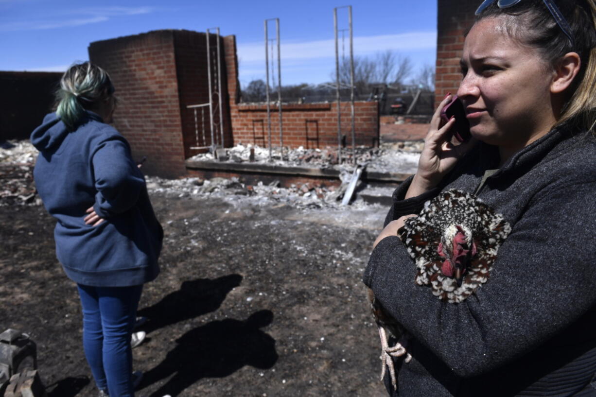 Priscilla Maynard holds a chicken while taking on the phone in front of a burned home Friday, March 18, 2022 near Carbon, Texas in Eastland County.  Fire crews in West Texas hope to make progress Saturday against a massive complex of wildfires that have killed one person and burned at least 50 homes, officials said.   (Ronald W.