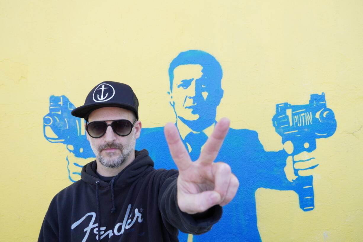 Street artist Todd Goodman, known as 1GoodHombre, stands in front of his stencil of Ukrainian President Volodymyr Zelenskyy holding submachine guns, painted without a permit on a building's wall in Santa Monica, Calif., on Monday, March 21, 2022. Goodman came out of anonymity as a street artist, risking arrest and fines for his unlicensed work to solicit funds for Ukrainian war refugees.