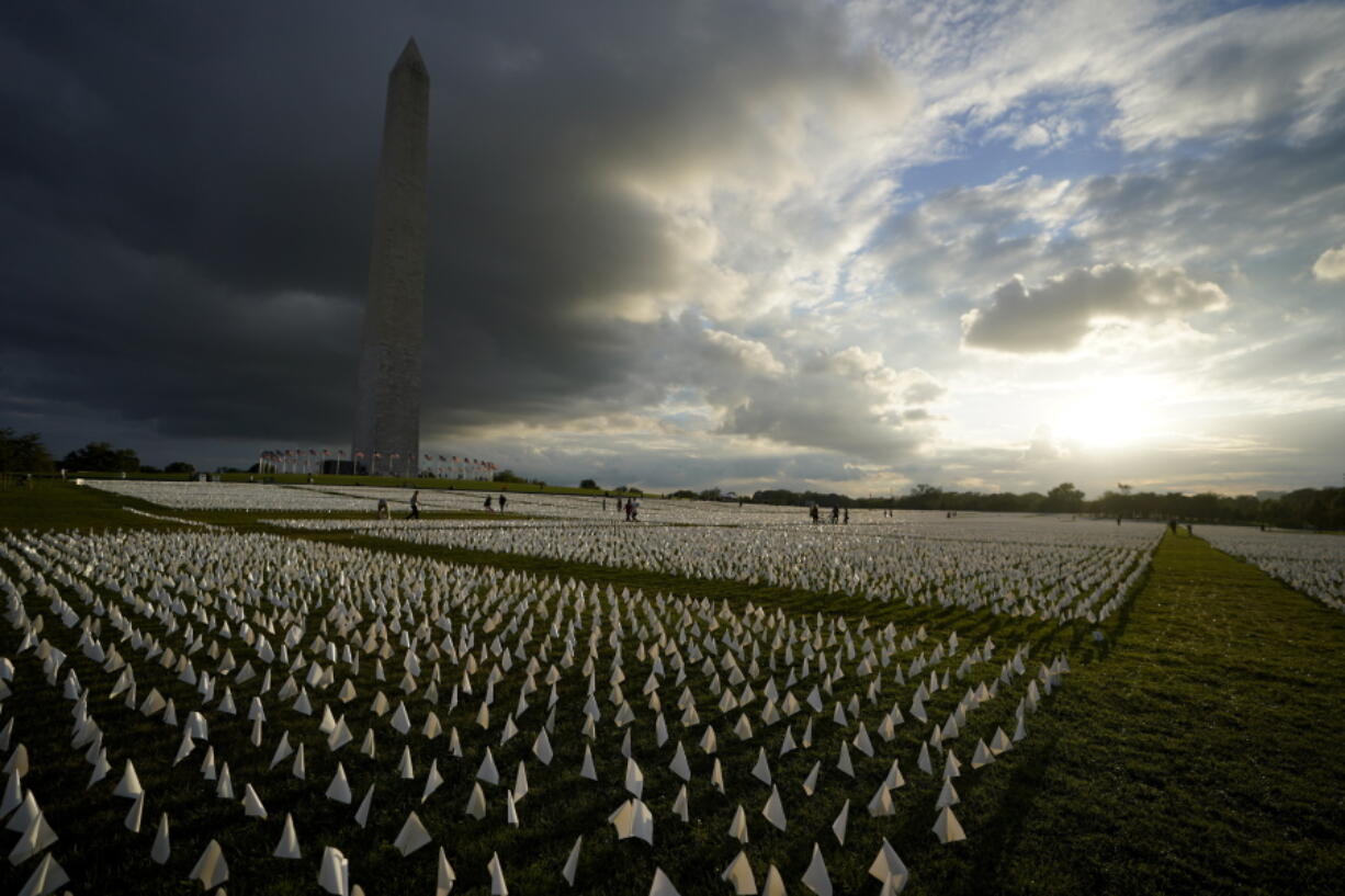 FILE - With the Washington Monument in the background, people look at white flags that are part of artist Suzanne Brennan Firstenberg's temporary art installation, "In America: Remember," in remembrance of Americans who have died of COVID-19, on the National Mall in Washington, Sept. 17, 2021. The installation consists of more than 630,000 flags. The federal government has provided more than $2 billion to help cover funeral costs for more than 300,000 families of people who died from COVID-19, the Federal Emergency Management Agency announced Tuesday as launches a new campaign to raise awareness for the aid to the families of the more than 965,000 people who have died in the U.S. from the virus.