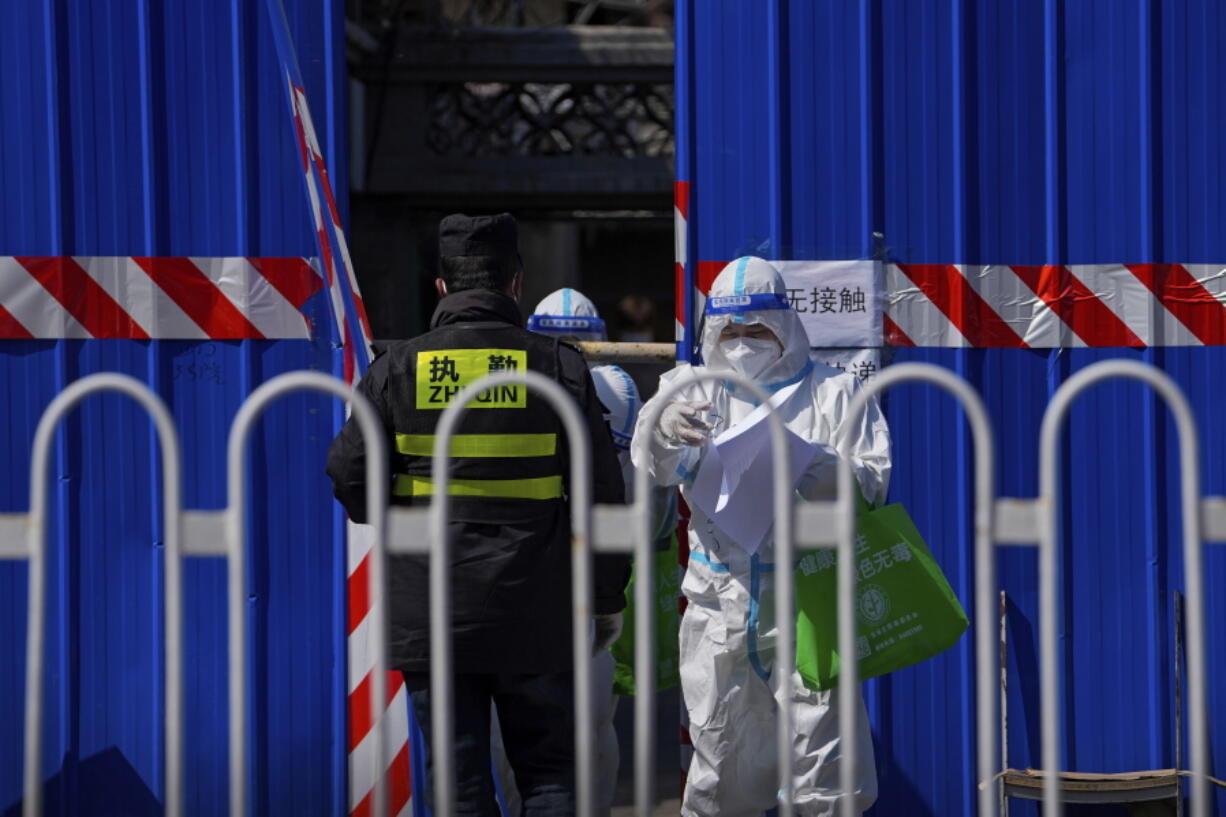 A health worker wearing a protective suit holds check lists as they walk out from a barricaded community which was locked down for health monitoring following the COVID-19 case detected in the area, Monday, March 28, 2022, in Beijing. China began its largest lockdown in two years Monday to conduct mass testing and control a growing outbreak in its largest city of Shanghai as questions are raised about the economic toll of the nation's "zero-COVID" strategy.