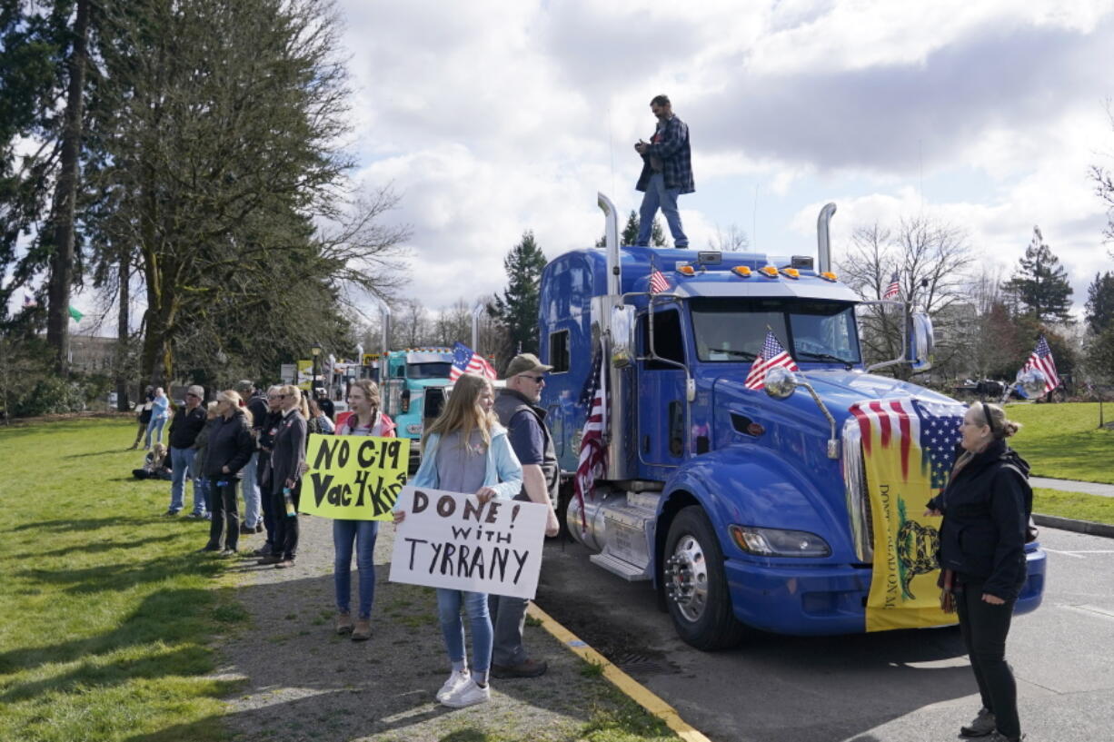 People hold signs as they stand near parked semi-trucks during a protest against COVID-19 vaccine mandates and other issues, Saturday, March 5, 2022, at the Capitol in Olympia, Wash. The trucks were part of a local convoy that traveled to Olympia for the protest. (AP Photo/Ted S.