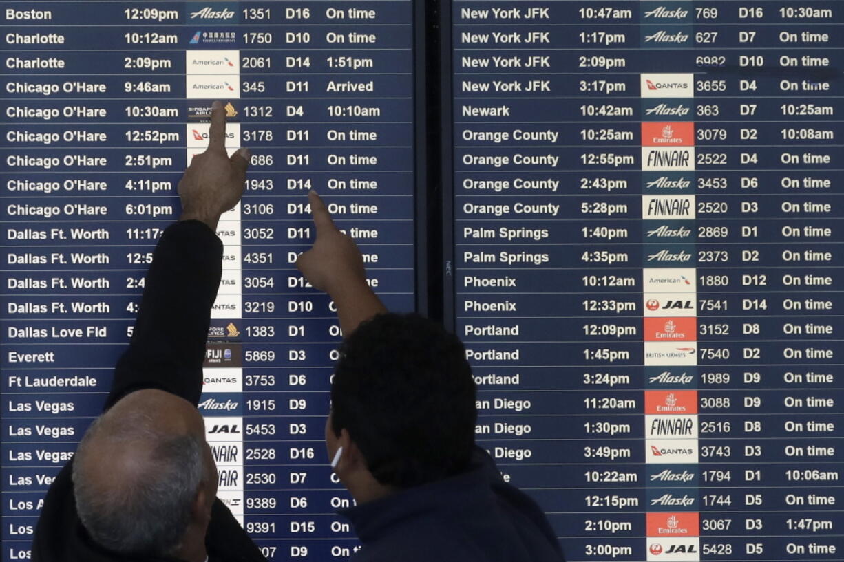 FILE - Two men point toward plane arrivals on a flight information board at San Francisco International Airport in San Francisco, Tuesday, Nov. 26, 2019.   Forecasters say, Friday, March 11, 2022,  a powerful, late-winter storm combining rivers of moisture and frigid temperatures is expected to dump snow from the Deep South all the way north to the Canadian border over the weekend that could cause travel problems and power outages across a wide part of the Eastern United States from late Friday through early next week.