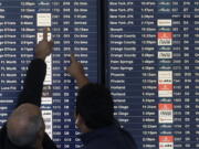 FILE - Two men point toward plane arrivals on a flight information board at San Francisco International Airport in San Francisco, Tuesday, Nov. 26, 2019.   Forecasters say, Friday, March 11, 2022,  a powerful, late-winter storm combining rivers of moisture and frigid temperatures is expected to dump snow from the Deep South all the way north to the Canadian border over the weekend that could cause travel problems and power outages across a wide part of the Eastern United States from late Friday through early next week.