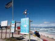 People sit next to shark-education signs, and the shark-warning flag at Muizenberg beach, which is part of False Bay in Cape Town, South Africa.