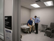 Rob Purdie, left, who has valley fever, checks in with his doctor at the same clinic where he serves as the Program Development Coordinator at the Valley Fever Institute at Kern Medical on March 22, 2022, in Bakersfield, California. Infectious Disease Physician Dr. Arash Heidari examines the port on Rob's head that is used to deliver medicine to treat his Valley Fever.