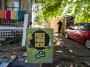 A sign greets visitors as Gretta Anderson looks over contents of the free food pantry and fridge at her Vancouver home Monday afternoon, Sept. 20, 2021. The Vancouver Free Fridge project is up to three fridges, but they're also being regulated by city codes over the structure, causing program leaders to start a petition.