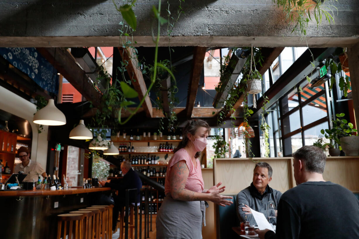 Server Virginia Samsel talks to customers about the drink menu at Light Sleeper on Capitol Hill on Friday, April 1, 2022, in Seattle, Washington.