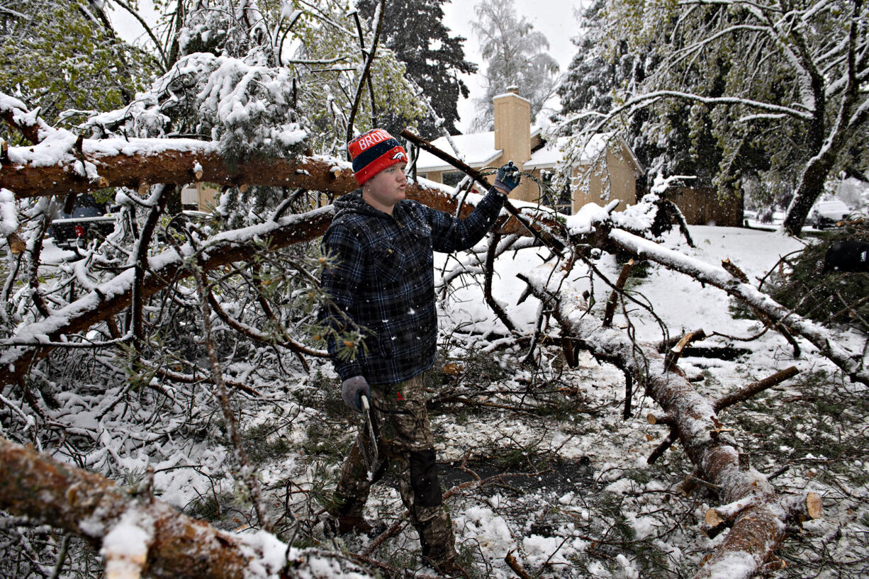 Ryan Dewater, 18, of Vancouver helps a neighbor clear a downed tree from their yard and the street after a rare April snowstorm hit the area Monday morning, April 11, 2022. Downed trees caused problems for residents and motorists on Monday.